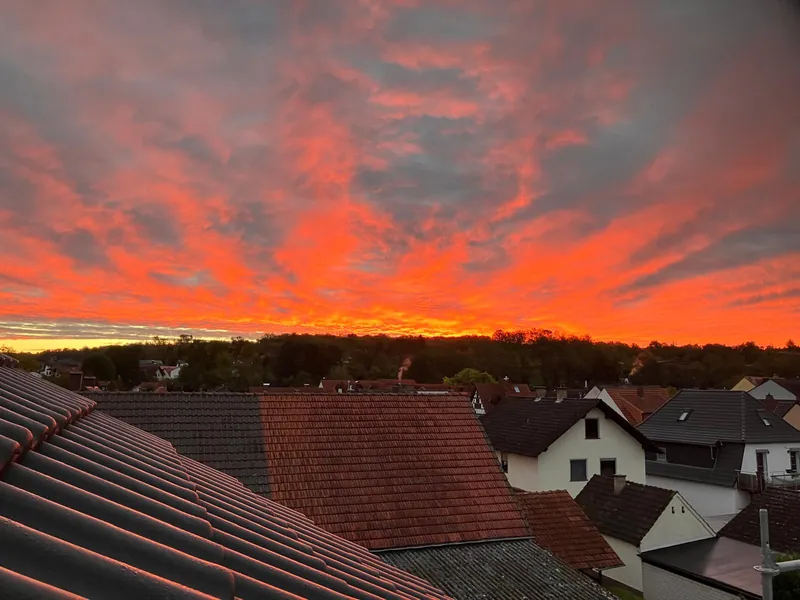 Leuchtend roter Abendhimmel über den Ziegeldächern einer Wohnsiedlung