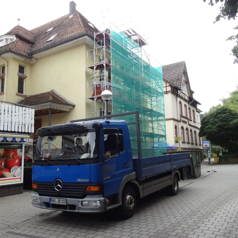Blauer Arens-LKW vor einem Altbau, dessen Ecke mit Gerüst und grünem Netz eingerüstet ist