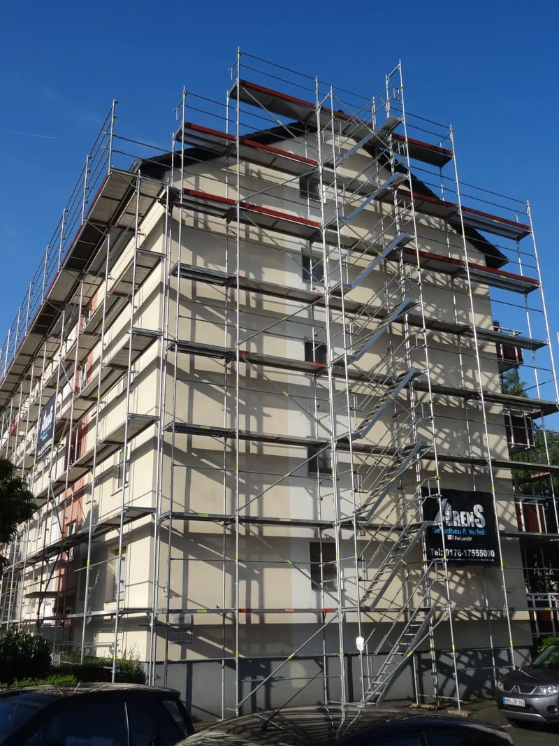Mehrgeschossiger Altbau, zwei Seiten bis unter das Dach eingerüstet, vor blauem Himmel