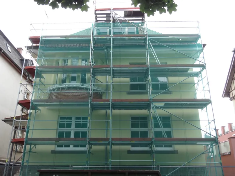 Altbaufassade, vollständig mit Gerüst und grünem Schutznetz eingehaust