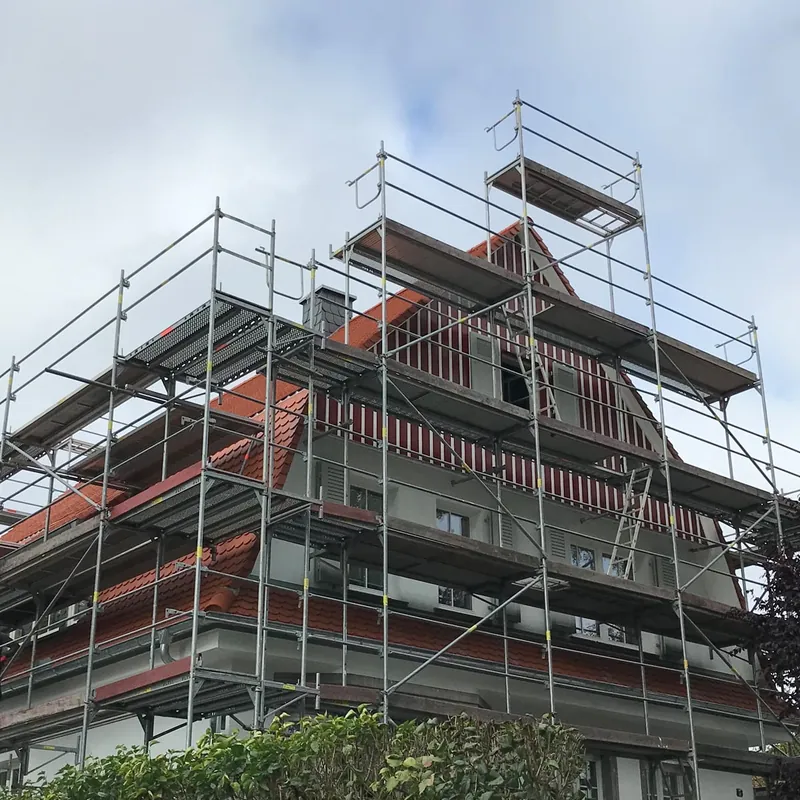 Hohes Wohnhaus mit steilem Giebel, rundum mit Gerüst und Dachfangschutz eingerüstet