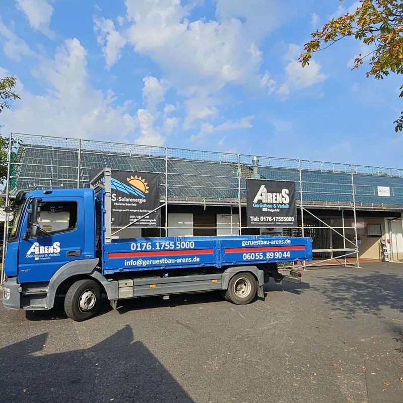 Blauer Arens-LKW vor einem eingerüsteten Flachbau mit Solarmodulen auf dem Dach