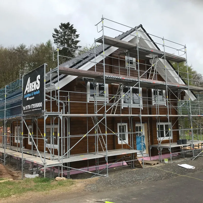 Holzhaus mit Satteldach, rundum eingerüstet, am Gerüst ein Arens-Banner