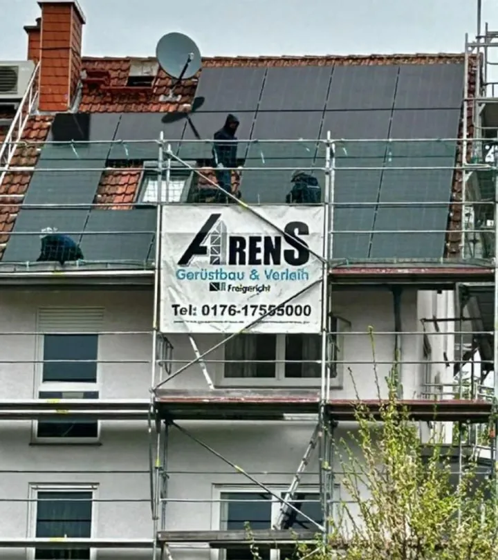 Wohnhaus mit Gerüst und Arens-Banner, auf dem Dach montieren Arbeiter Solarmodule
