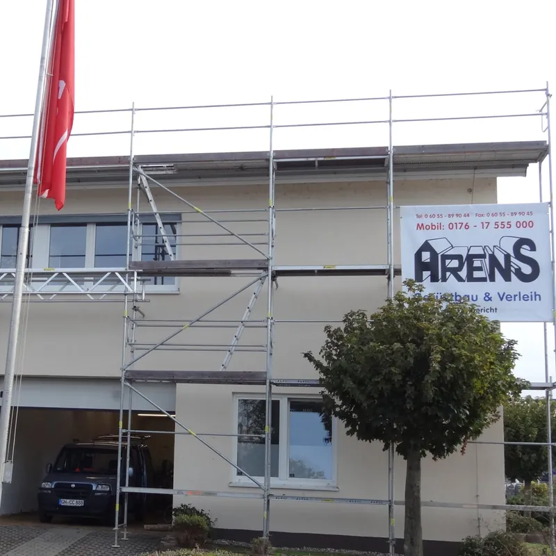 Hell verputztes Haus über einer Garage mit Gerüst und Arens-Banner