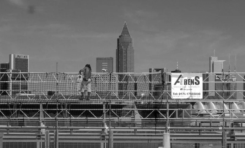 Schwarz-weiß-Foto: Arbeiter auf einem Gerüst mit Arens-Banner, im Hintergrund die Frankfurter Skyline